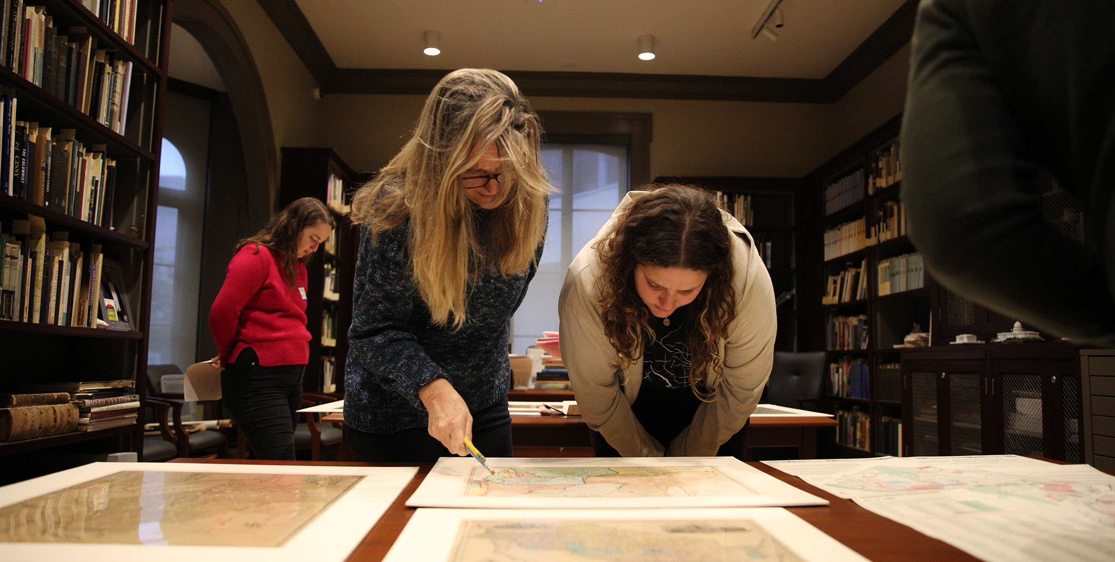 Two women leaning over to look at paper maps 