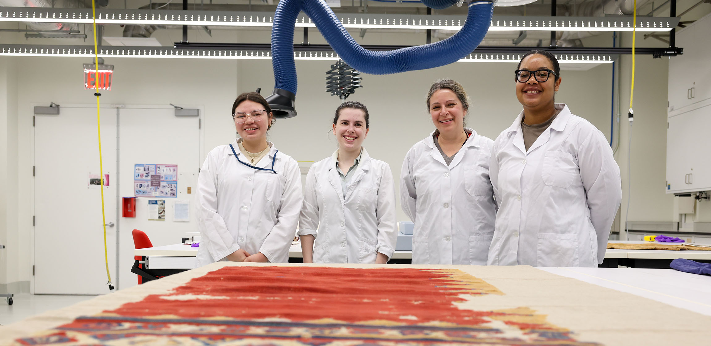 Four women in lab coats smile in a conservation lab